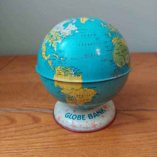 A vintage globe with a blue ocean map and yellow/green landmasses, displayed on a white round base printed with 'GLOBE BANK' and set on a wooden tabletop.