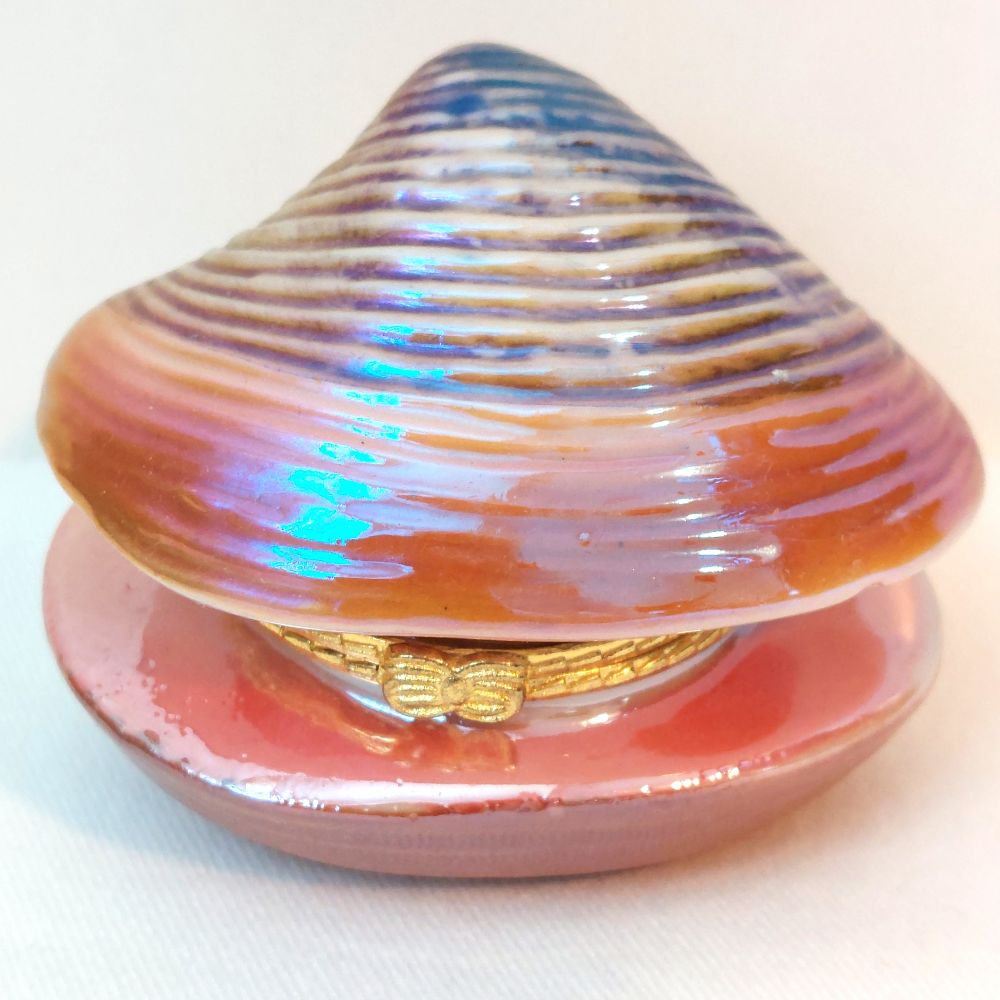 A decorative clam shell-shaped jewelry box with a glossy finish, featuring iridescent blue and purple highlights, a peach and pink exterior, and a gold bow detail on the front.
